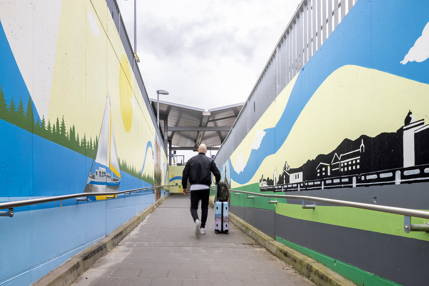 Ein Mann mit Koffer lauft an der Station Erftstadt entlang. Rechts und links von ihm ist Kunstgraffiti zu sehen.