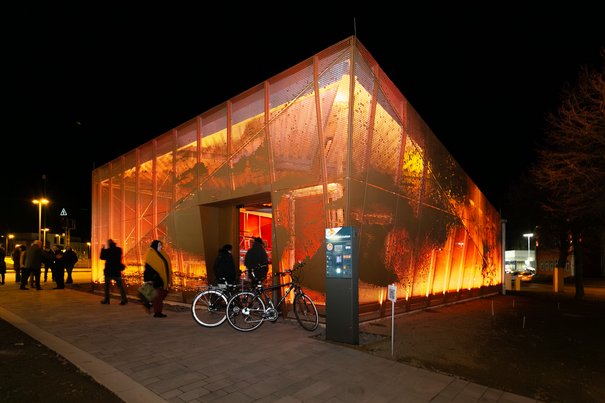 Das neue Fahrradparkhaus begrüßt die Menschen am Bedburger Bahnhof mit einer künstlerisch gestalteten und in den Abendstunden beleuchteten Fassade. © Hannes Keßler, Stadt Bedburg