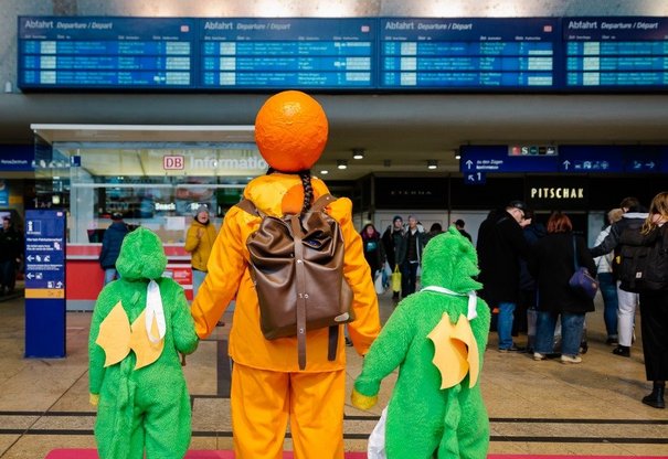 Kostümierte Menschen stehen vor Fahrtzielanzeige im Kölner Hbf