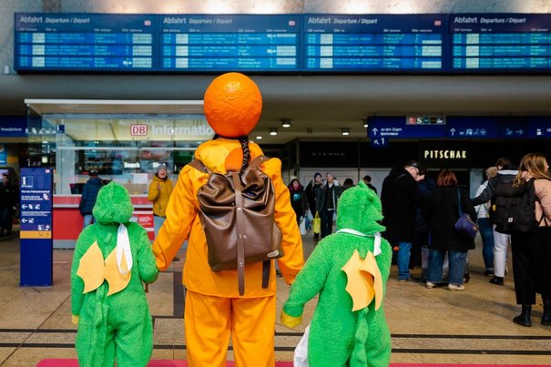 Kostümierte Menschen stehen vor Fahrtzielanzeige im Kölner Hbf